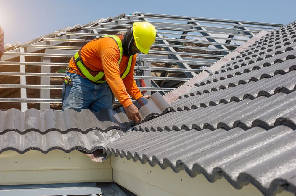 A roofing professional in white gloves replaces gray tiles or shingles on a house, set against a clear blue sky. Ideal for showcasing roofing and construction services.