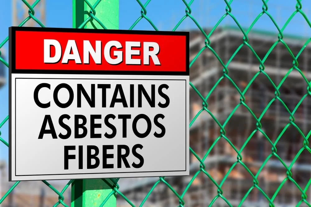 A warning signboard and protective metal netting highlight the hazardous asbestos fibers at a construction site, emphasizing safety and restricted access.