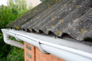 Close-up of house asbestos roof with gutter holder and plastic roof gutter pipe.