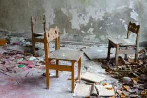 Abandoned kindergarten with small wooden school chairs amidst dirt and debris