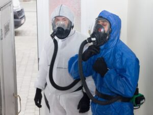 Asbestos removal work is underway on heating pipe insulation in the basement, with all walls covered in plastic and filtered air extraction to eliminate every fiber.