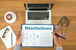 Mesothelioma doctor writing medical records on a clipboard. Top view with medical equipment, a desktop, and a coffee cup in the background.