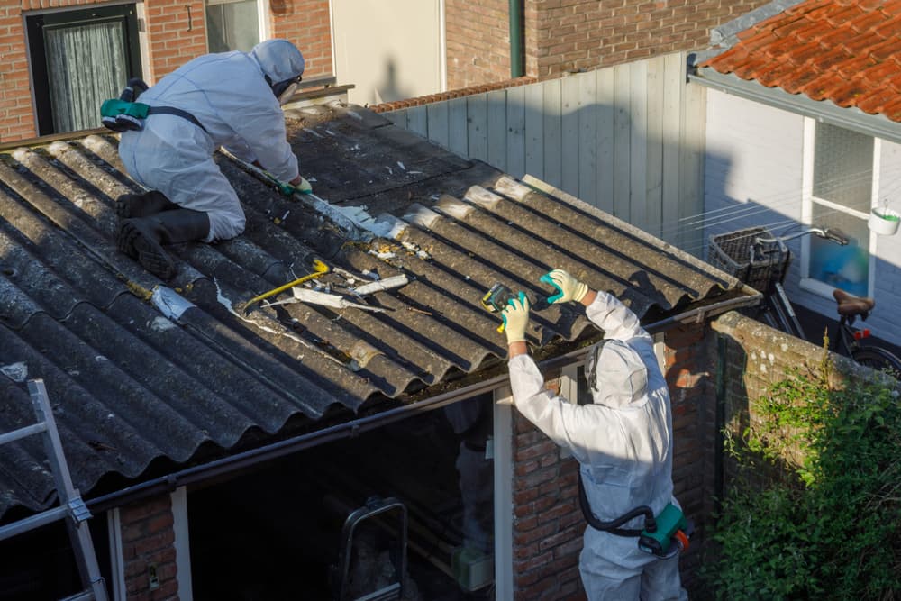 Men in protective suits are removing asbestos cement corrugated roofing