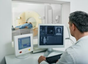 A radiologist operates a CT scan from the control room, focusing on the patient's lung examination using computed tomography.