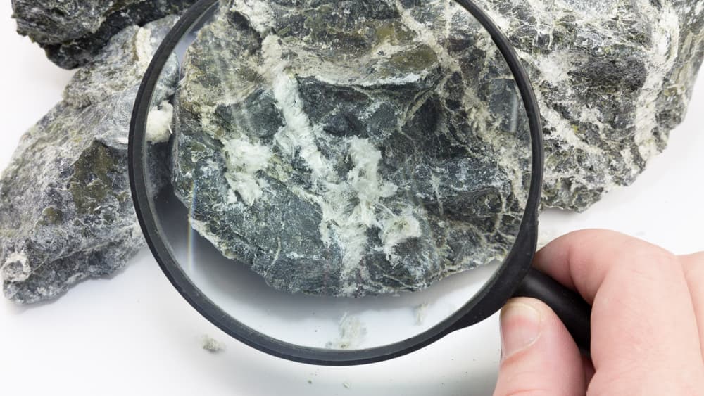 Hand with magnifying glass examines asbestos fibers in stone