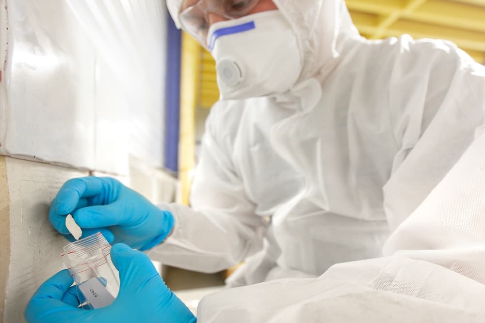 Asbestos surveyor taking a sample of building material in small plastic bag