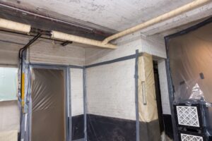 Asbestos removal works off heating pipes insultation going on in a basement with all walls covered in plastic and filtered air extraction to remove every fiber